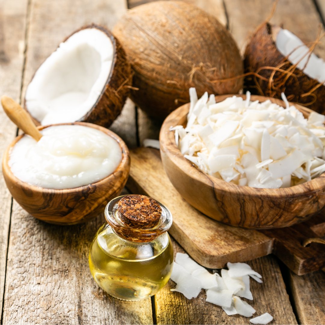 Coconut oil bottle, coconuts, and coconut pieces on a wooden surface